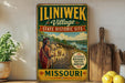 A vintage-style metal sign for the "ILINIWAK Village" in Missouri, featuring a painting of a Native American village and the text "ILINIWAK Village State Historic Site" and "Missouri".
