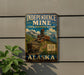 A vintage-style metal sign for Independence Mine, a state historical park in Alaska, featuring a train and a mountain landscape.