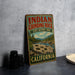 A vintage-style sign for Indian Grinding Rock State Historic Park in California, featuring a scenic landscape with a river and mountains.