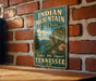 A vintage metal sign for Indian Mountain State Park in Tennessee, featuring a scenic landscape with mountains, trees, and a lake.