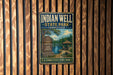 A vintage metal sign for Indian Well State Park in Connecticut, featuring a scenic landscape with a lake, trees, and a gazebo.