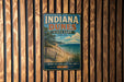 A vintage-style metal sign for Indiana Dunes State Park, featuring a beach scene with a lake and a cloudy sky.