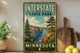 A vintage-style sign for Interstate State Park in Minnesota, featuring a scenic landscape with a river, pine trees, and mountains.