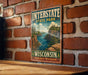 A vintage metal sign for Interstate State Park in Wisconsin, featuring a scenic landscape with a river and mountains.