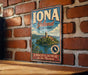 A vintage-style metal sign for Iona Island, New York, featuring a scenic illustration of the island and its surroundings.