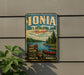 A vintage-style metal sign for the Ionia State Recreation Area in Michigan, featuring a scenic image of a lake, pine trees, and a red canoe.