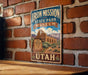 A vintage-style metal sign for Iron Mission State Park Museum in Utah, featuring an illustration of a historic building surrounded by desert vegetation.
