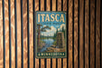 A vintage metal sign for Itasca State Park in Minnesota, featuring a scenic landscape with a river, pine trees, and a monument.