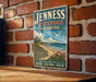 A vintage-style metal sign for "Jenessa State Beach, New Hampshire" is displayed on a brick wall, featuring a beach scene with a lighthouse and a bird in flight.