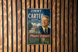 A vintage-style metal sign featuring a portrait of former President Jimmy Carter, with text promoting the National Historical Park in Plains, Georgia.