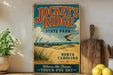 A vintage-style sign for Jockey's Ridge State Park in North Carolina, featuring a beach scene with a hang glider in the sky.