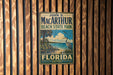 A vintage metal sign for John D. Mac Arthur Beach State Park in Florida, featuring a beach scene with palm trees and a bird.