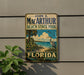 A vintage-style sign for John D. Mac Arthur Beach State Park in Florida, featuring a beach scene with palm trees and a heron.