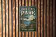 A vintage metal sign for John Hens Park in Wisconsin, featuring a scenic landscape with a lake and pine trees.