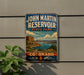 A vintage-style sign for John Martin Reservoir, a state park in Colorado, featuring a scenic landscape with mountains, water, and a cloudy sky.