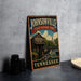 A vintage-style metal sign for Johnsonville State Historic Park in Tennessee, featuring a wooden building and a watermill, is displayed on a gray countertop.