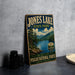 A vintage-style sign for Jones Lake State Park, featuring a scenic landscape with pine trees, a lake, and mountains in the background.