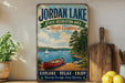 A vintage-style sign for Jordan Lake, North Carolina, featuring a scenic image of a lake with a sailboat, surrounded by pine trees and a wooden dock.