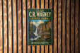 A vintage metal sign for C.R. Magney State Park in Minnesota, featuring a scenic image of a waterfall surrounded by pine trees.