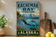 A vintage-style sign for Kachamak Bay State Park in Alaska, featuring a scenic landscape with a bald eagle, mountains, and a lake with a boat.
