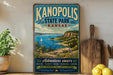 A vintage-style metal sign for Kanopolis State Park in Kansas, featuring a scenic landscape with a lake, mountains, and a sailboat.