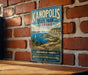 A vintage-style metal sign for Kanopolis State Park in Kansas, featuring a scenic landscape with a lake, mountains, and a sailboat.