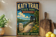 A vintage-style metal sign for Katy Trail State Park in Missouri, featuring a scenic illustration of a bridge, path, and surrounding landscape.