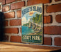 A vintage-style metal sign for Kelley's Island, Ohio, featuring a scenic landscape with a lake, cliffs, and trees.
