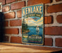 A vintage-style sign for Kenlake State Resort Park in Kentucky, featuring a scenic illustration of a lake with a sailboat and mountains in the background.