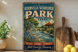 A vintage-style sign for Kerrville Schreiner Park in Texas, featuring a scenic illustration of a river, bridge, and surrounding nature.