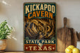 A vintage-style metal sign for the Kickapoo Cave in State Park, Texas, featuring an illustration of the cave and the text "KICKAPOO CAVEN" in a decorative font.