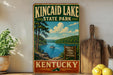 A vintage-style metal sign for Kincaid Lake State Park in Kentucky, featuring a scenic landscape with a lake, mountains, and a boat.