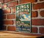 A vintage metal sign for Kings Mountain State Park in South Carolina, featuring a scenic landscape with a tree and rocks.
