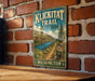 A vintage-style metal sign for Klickitat Trail, located in Washington State Park, is displayed on a brick wall.