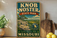 A vintage-style sign for Knob Noster State Park in Missouri, featuring a scenic landscape with mountains and a river.