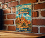 A vintage-style metal sign displaying the name "Kodachrome Basin State Park" and the location "UTAH" is mounted on a brick wall.