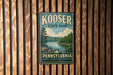 A vintage metal sign for Kooser State Park in Pennsylvania, featuring a scenic landscape with a lake and mountains.