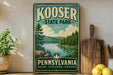 A vintage-style metal sign for Kooser State Park in Pennsylvania, featuring a scenic landscape with a lake and forest.
