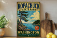 A vintage-style sign for Kopachuck State Park in Washington, featuring a scenic landscape with a lake, pine trees, and mountains.