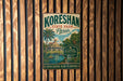 A vintage metal sign for Koreshan State Park in Florida, featuring a tropical landscape with palm trees and a building, is displayed on a wooden wall.