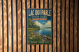 A vintage metal sign for Lacqui Parle State Park in Minnesota, featuring a scenic landscape with a lake, flowers, and a cloudy sky.