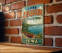 A vintage-style sign for Lake Ahwatukee State Park in Iowa, featuring a scenic image of a lake with a canoe and a sailboat.