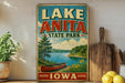 A vintage-style sign for Lake Anita State Park in Iowa, featuring a scenic illustration of a lake, canoe, and surrounding landscape.