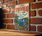 A vintage-style metal sign for Lake Arrowhead State Park in Texas, featuring a scenic landscape with a lake, mountains, and a sailboat.