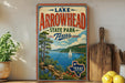 A vintage-style poster advertising Lake Arrowhead State Park in Texas, featuring a scenic landscape with a lake, mountains, and a sailboat.