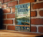 A vintage-style metal sign for Lake Bruin State Park in Louisiana, featuring a scenic image of a lake, boats, and trees.