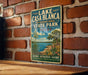 A vintage-style metal sign for Lake Casa Blanca, an international park in Texas, featuring a scenic landscape with a lake, desert, and cacti.