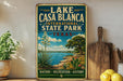A vintage-style sign for Lake Casa Blanca, an international state park in Texas, featuring a scenic landscape with a lake, cactus, and other natural elements.