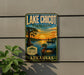 A vintage-style sign for Lake Chicot State Park in Arkansas, featuring a sunset scene with a duck and a palm tree.