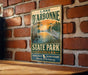 A vintage-style sign for Lake D'Arbonne State Park in Louisiana, featuring an illustration of a bird and a sunset over a body of water.